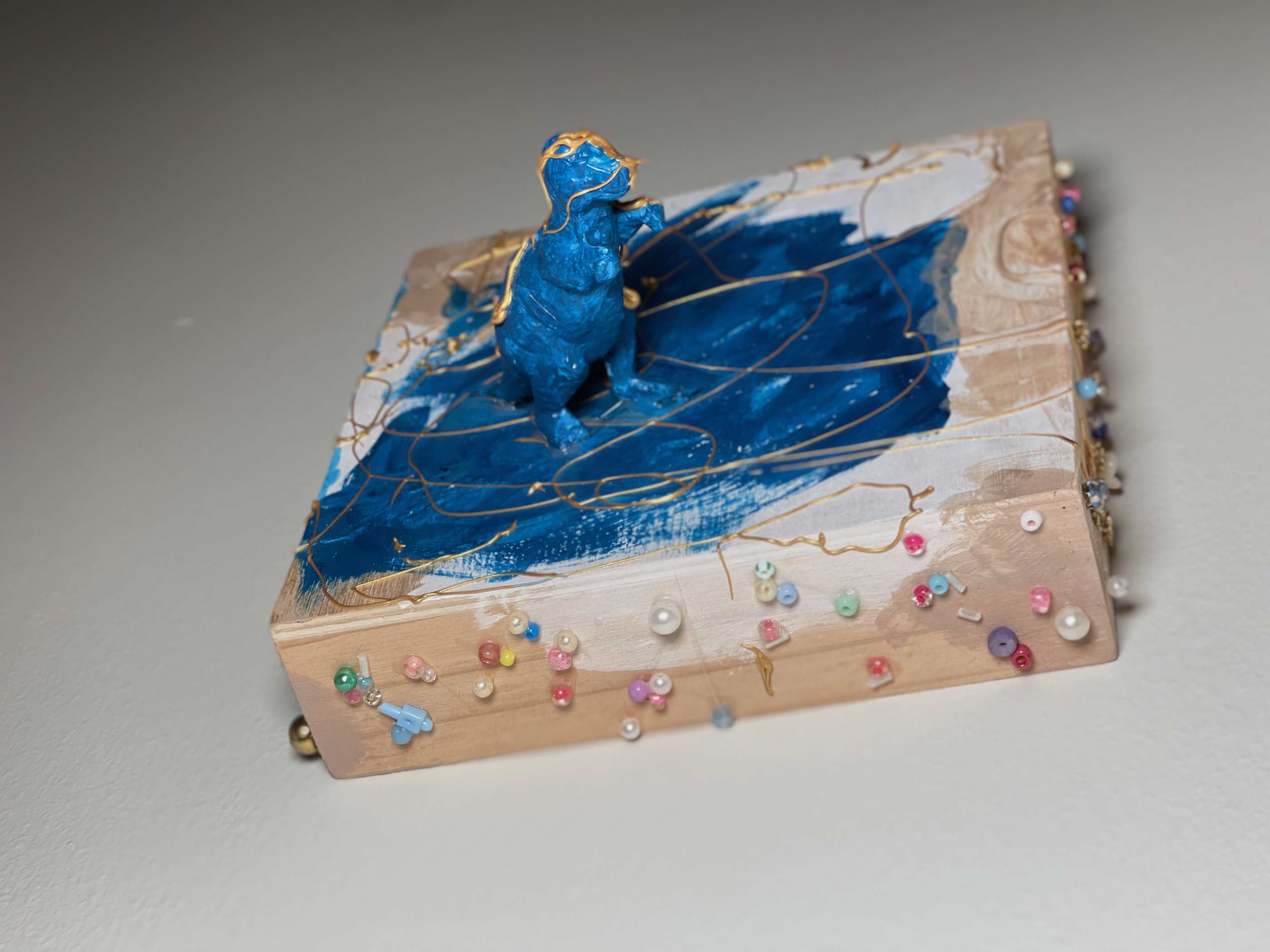A bright blue dinosaur figure standing on a painted and beaded wooden box