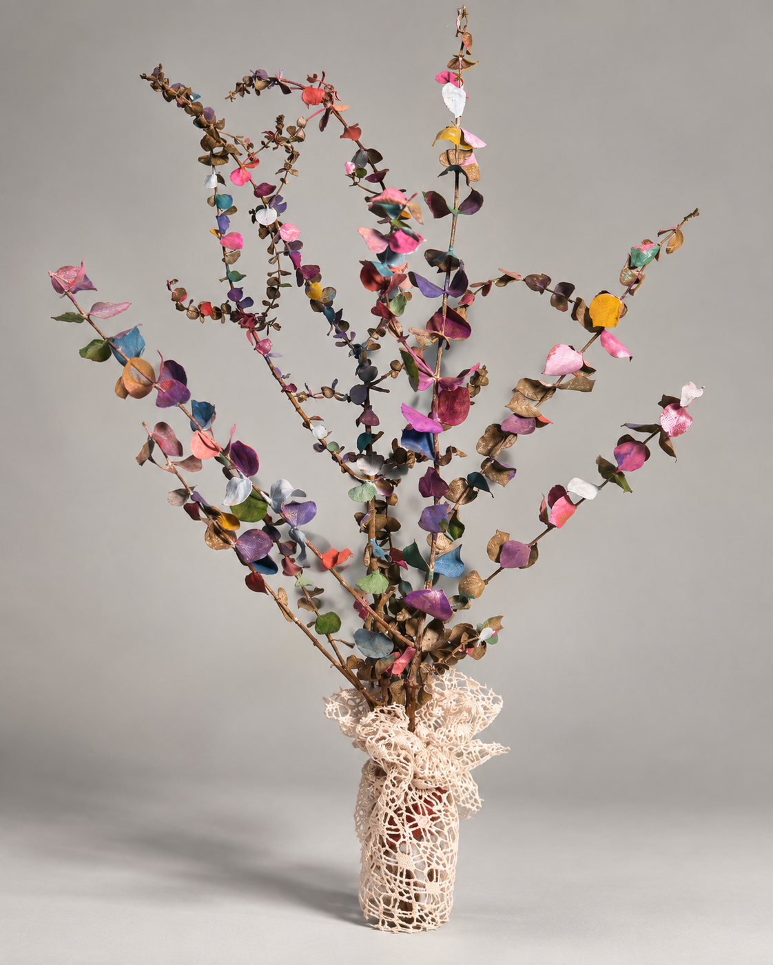 Full view of painted eucalyptus branches arranged in a lace-wrapped vessel