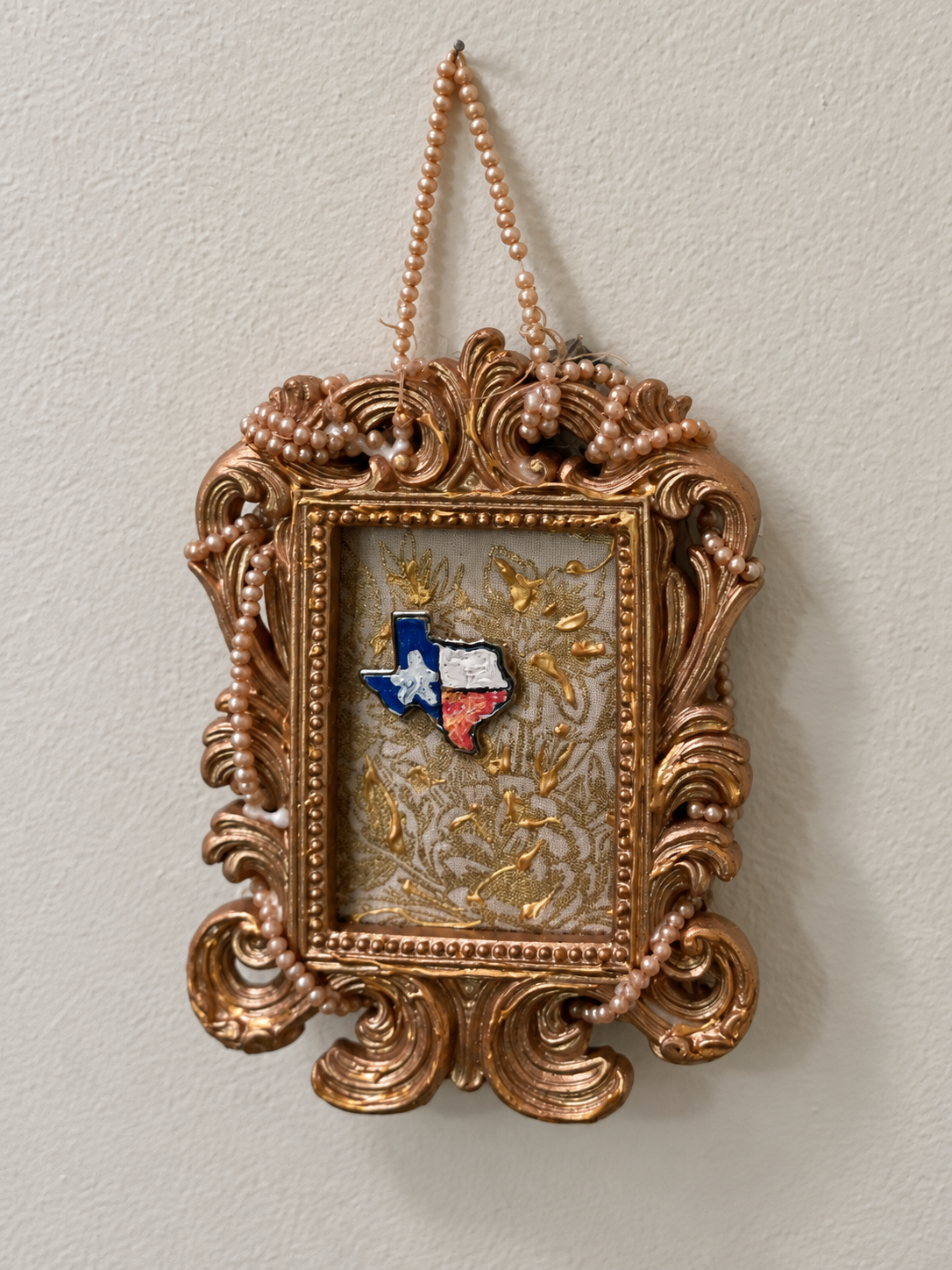 An ornate gold frame decorated with pearls and a small Texas-shaped element